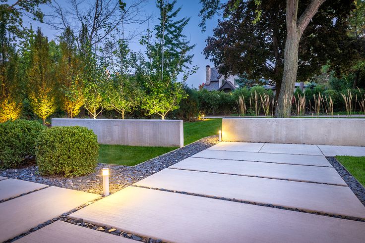 an outdoor walkway lit up at night with lights on the ground and trees in the background