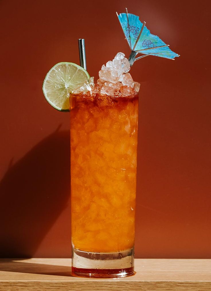 a drink with ice, lime and a butterfly on the top in front of a red wall