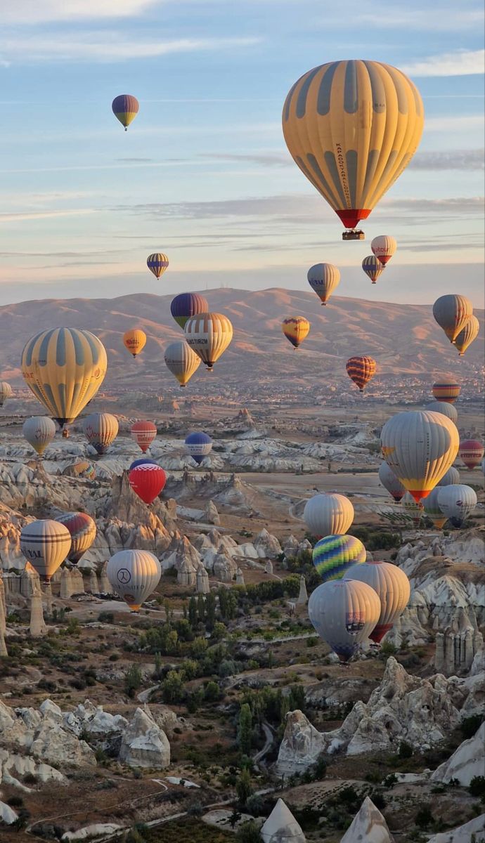 many hot air balloons are flying in the sky over rocks and boulders, with mountains in the background