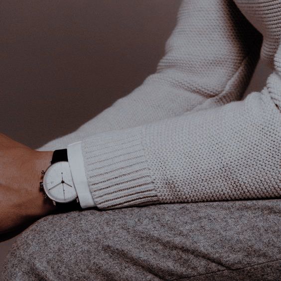 a person wearing a watch on their wrist and sitting down with his arm wrapped in a sweater