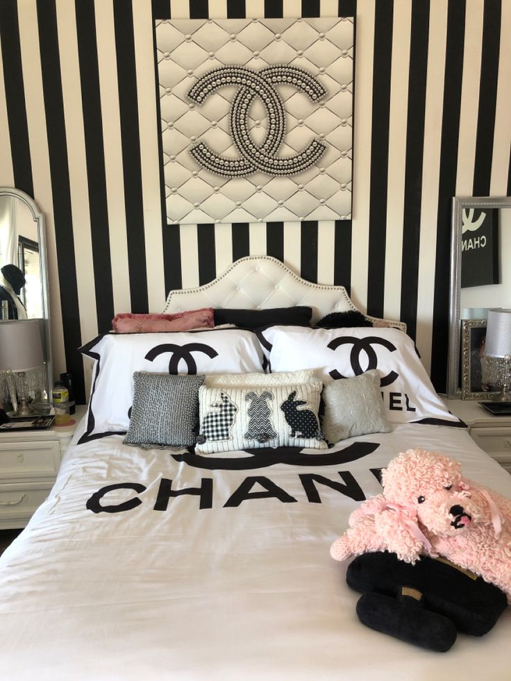 a bedroom with chanel wallpaper and black and white bedding, pink teddy bear