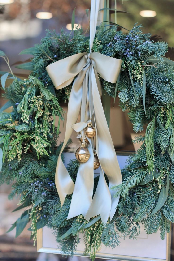 a christmas wreath hanging from the side of a building with bells and greenery on it