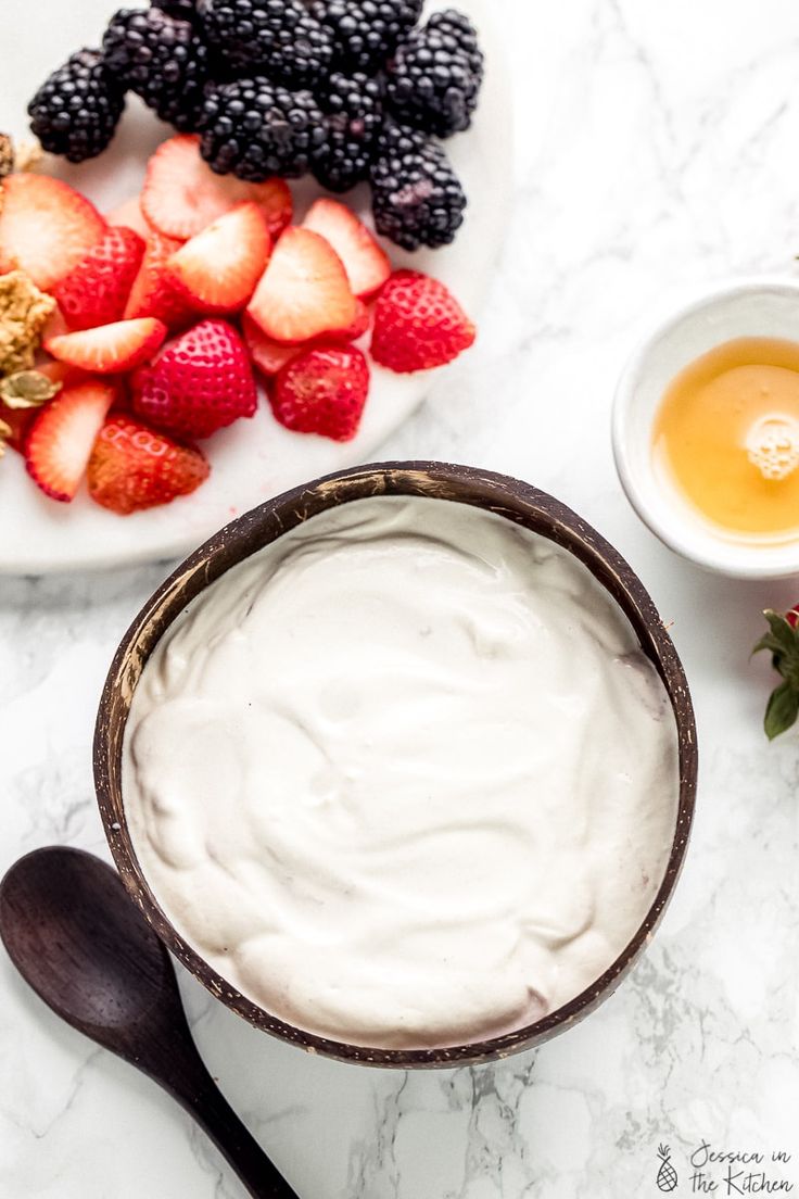 some fruit and yogurt are sitting on a marble counter top with spoons