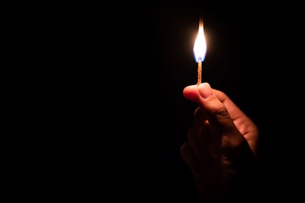 a person holding a lit matchstick in their right hand, with the light on