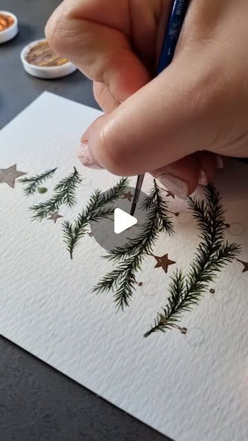 someone is drawing christmas trees on paper with pencils and watercolor pens while another person holds a pen