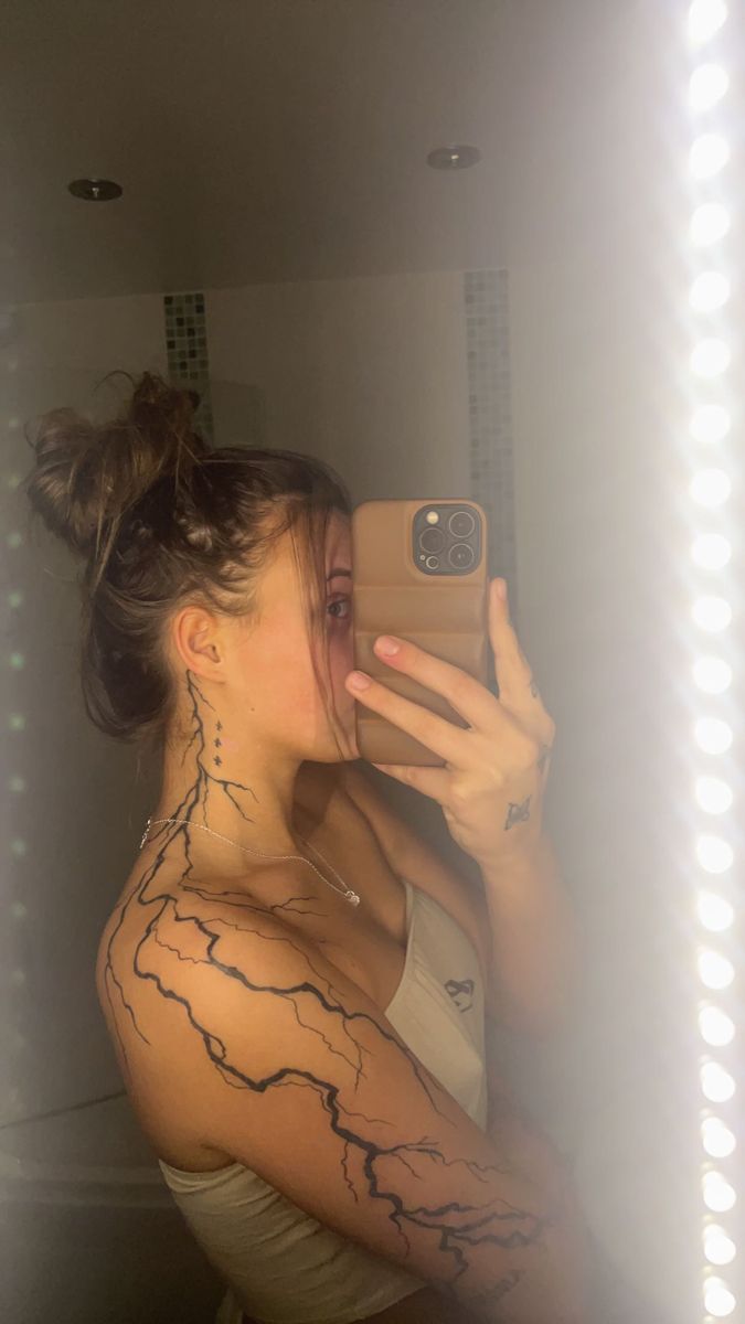 a woman taking a selfie in the mirror with her cell phone and tattoos on her arm