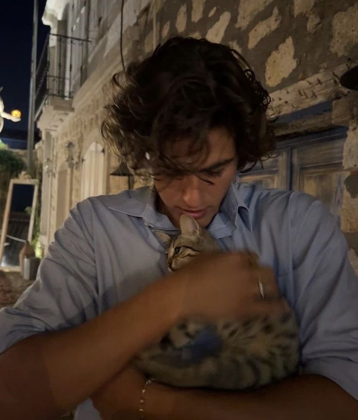 a man is holding a cat in his arms and looking down at it's neck