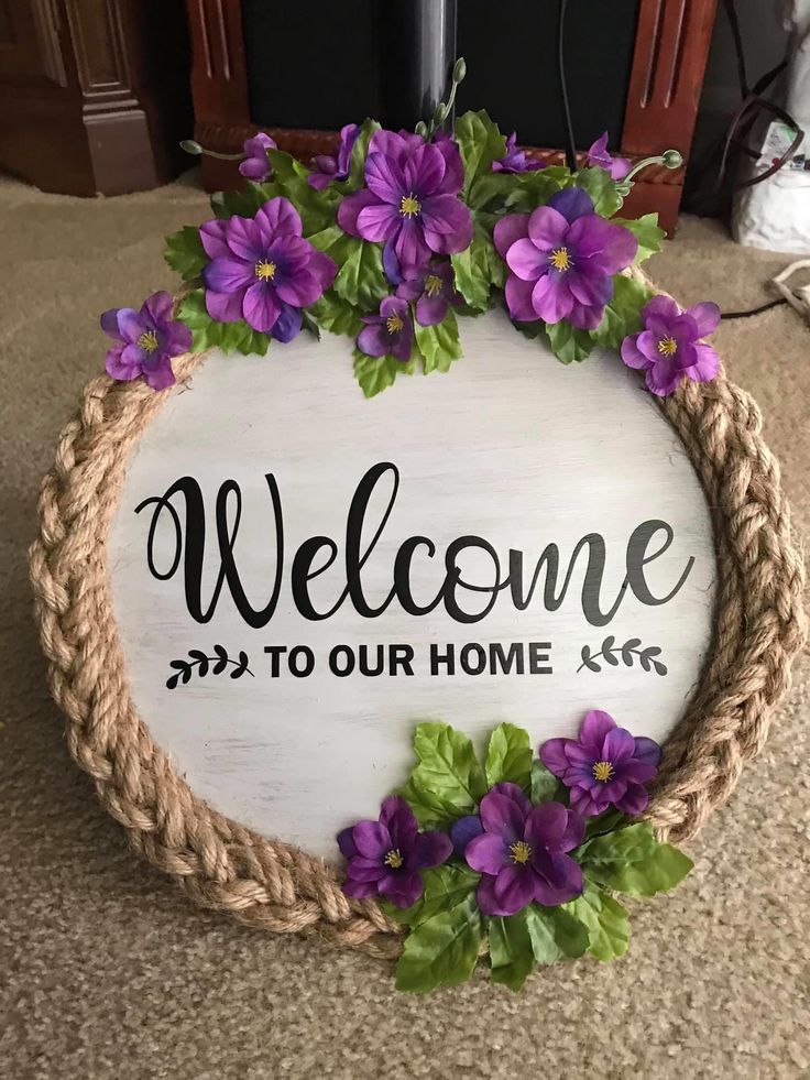 a welcome sign with purple flowers on the front and bottom is hanging from a rope