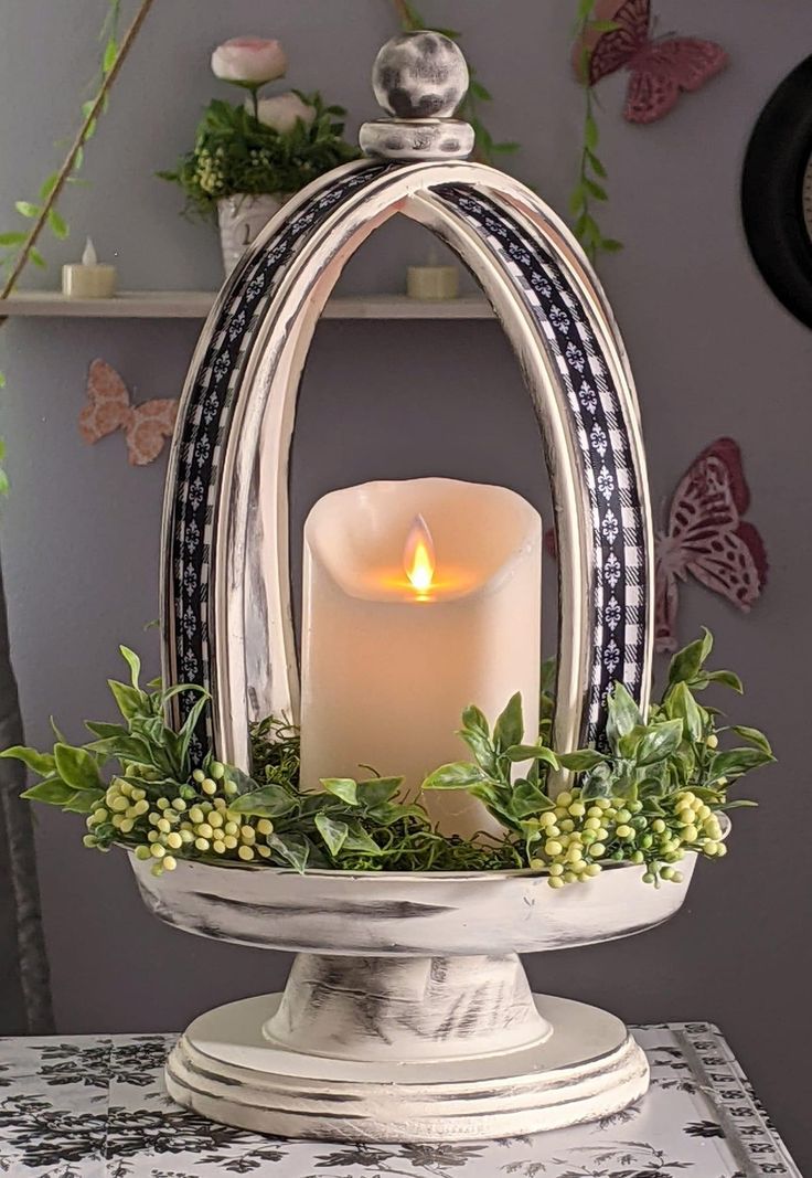 a lit candle is sitting in a bowl with greenery on the table next to it