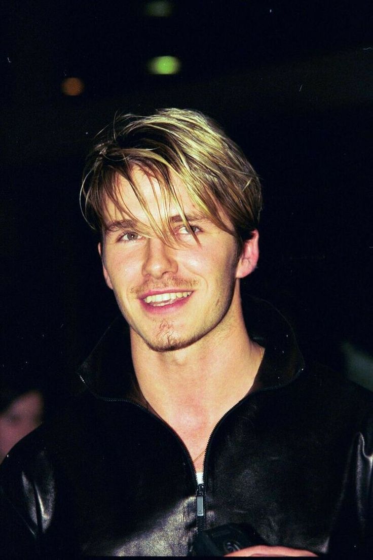 a young man with blonde hair wearing a black leather jacket and smiling at the camera