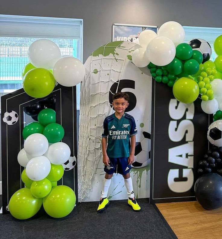 a young boy is standing in front of balloons and soccer goalie's arch