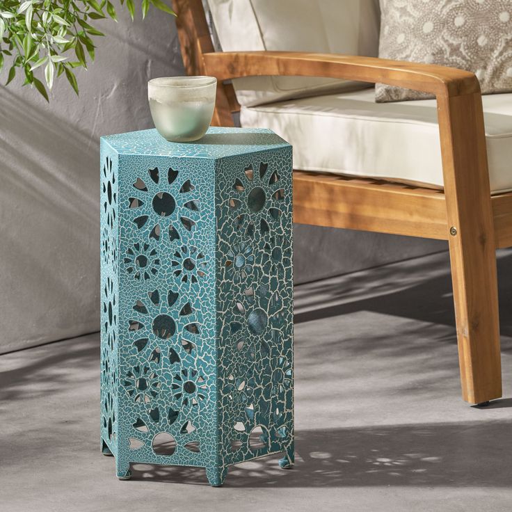 an outdoor side table with a bowl on it and a chair in the back ground