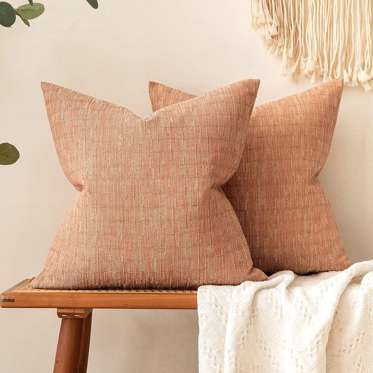 two brown pillows sitting on top of a wooden bench next to a wall hanging with plants