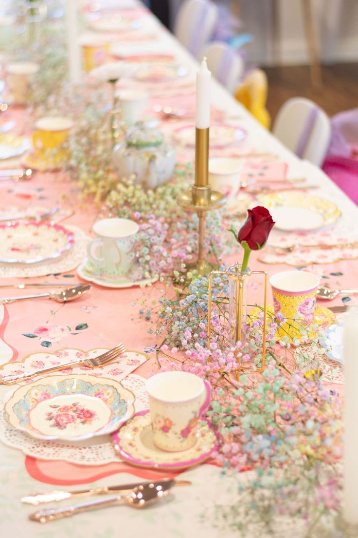 a long table is set with pink and gold plates, silverware, candlesticks and flowers