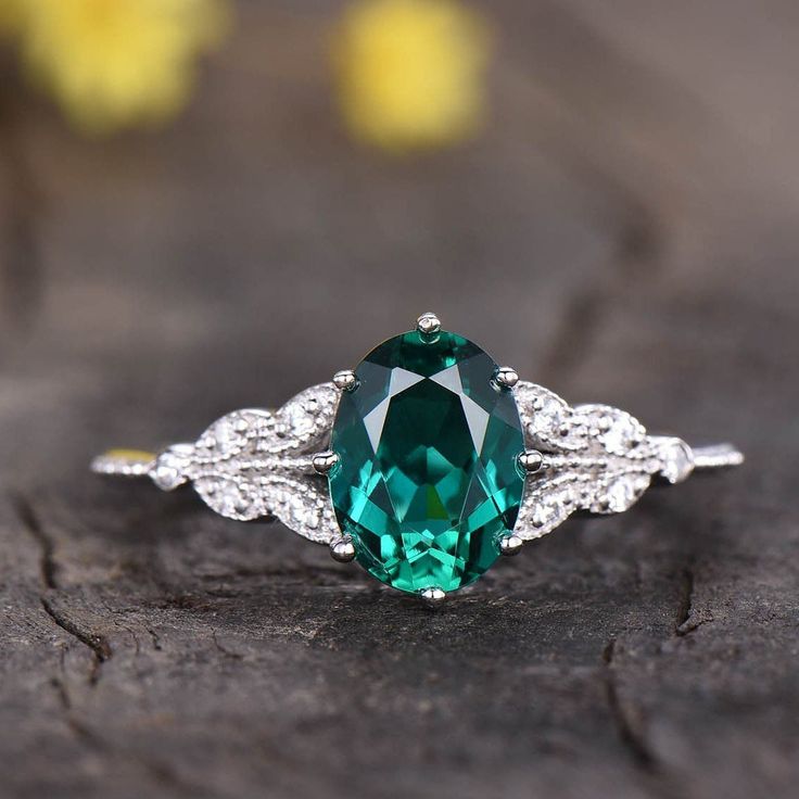 a green and white diamond ring sitting on top of a piece of wood with yellow flowers in the background