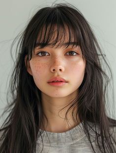 a woman with long hair and freckled bangs looks at the camera while wearing a gray shirt