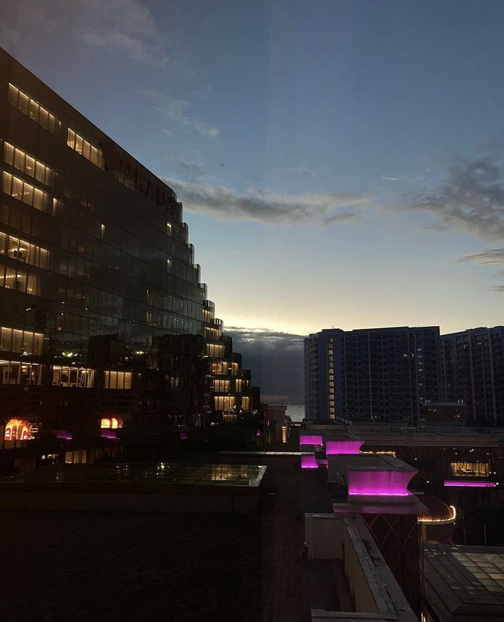 the city skyline is lit up at night with purple lights and buildings in the background