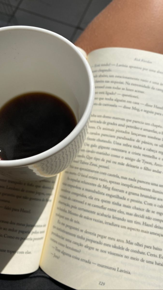 a cup of coffee sitting on top of an open book next to a person's arm