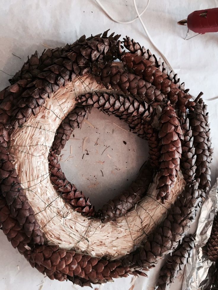 a wreath made out of pine cones sitting on top of a sheet of paper next to scissors