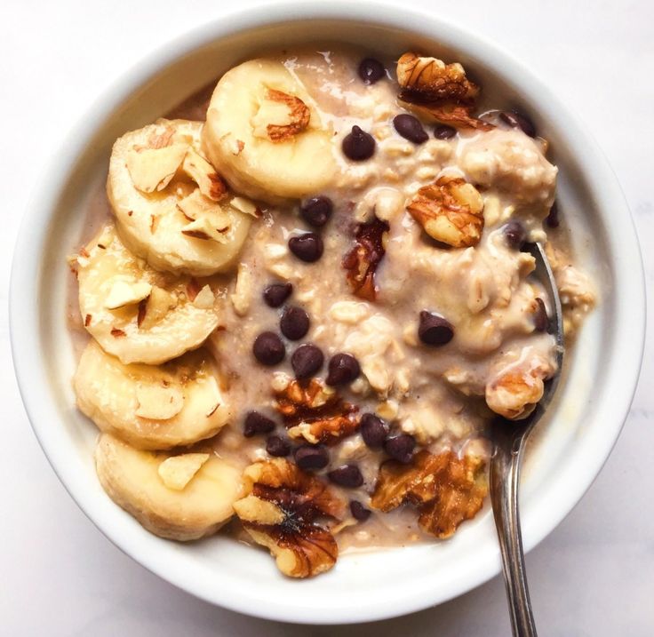 a bowl filled with oatmeal, bananas and raisins next to a spoon