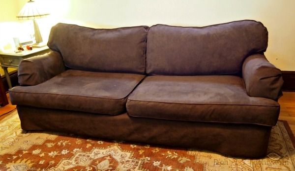 a brown couch sitting on top of a wooden floor next to a lamp and rug