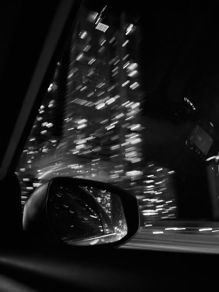 a car's rear view mirror is shown in the dark with city lights behind it