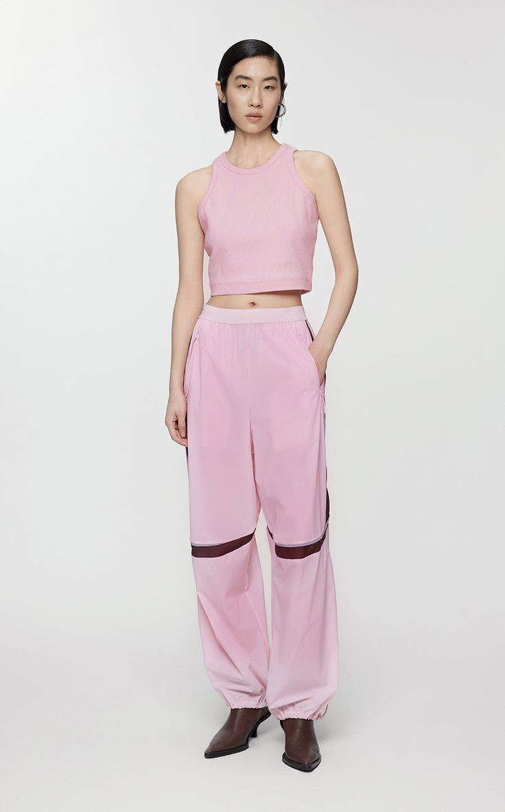 a woman standing in front of a white background wearing pink pants and a crop top