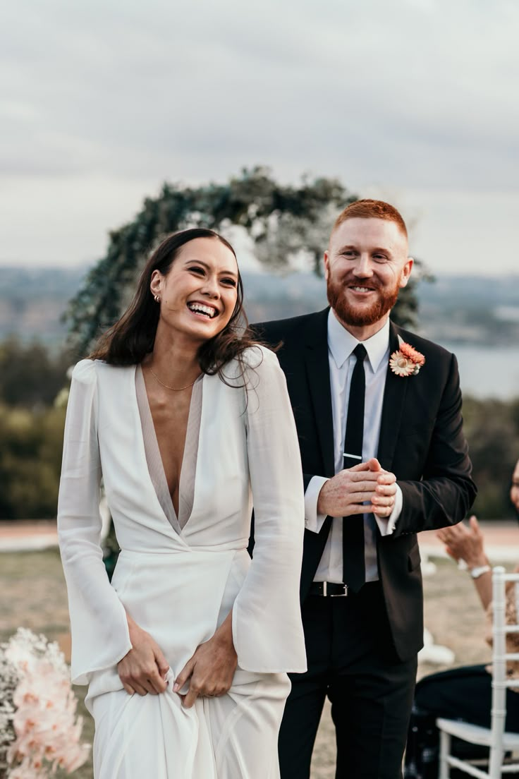 a bride and groom smile as they walk down the aisle at their outdoor wedding ceremony