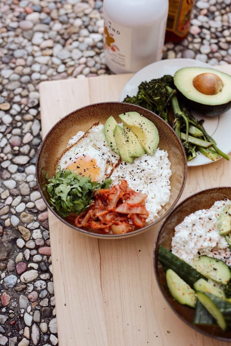 two bowls filled with food sitting on top of a wooden cutting board next to an avocado