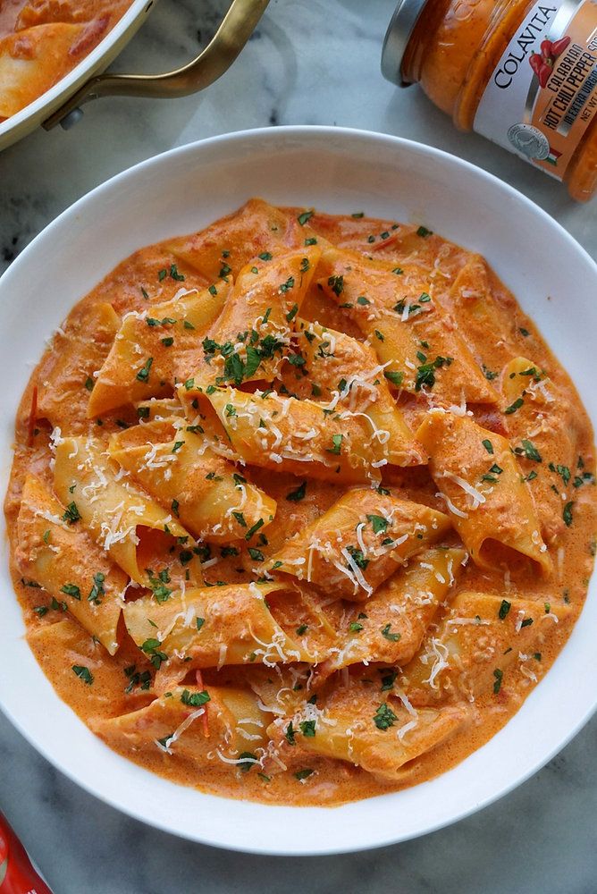 a white bowl filled with pasta and sauce on top of a marble table next to a bottle of beer