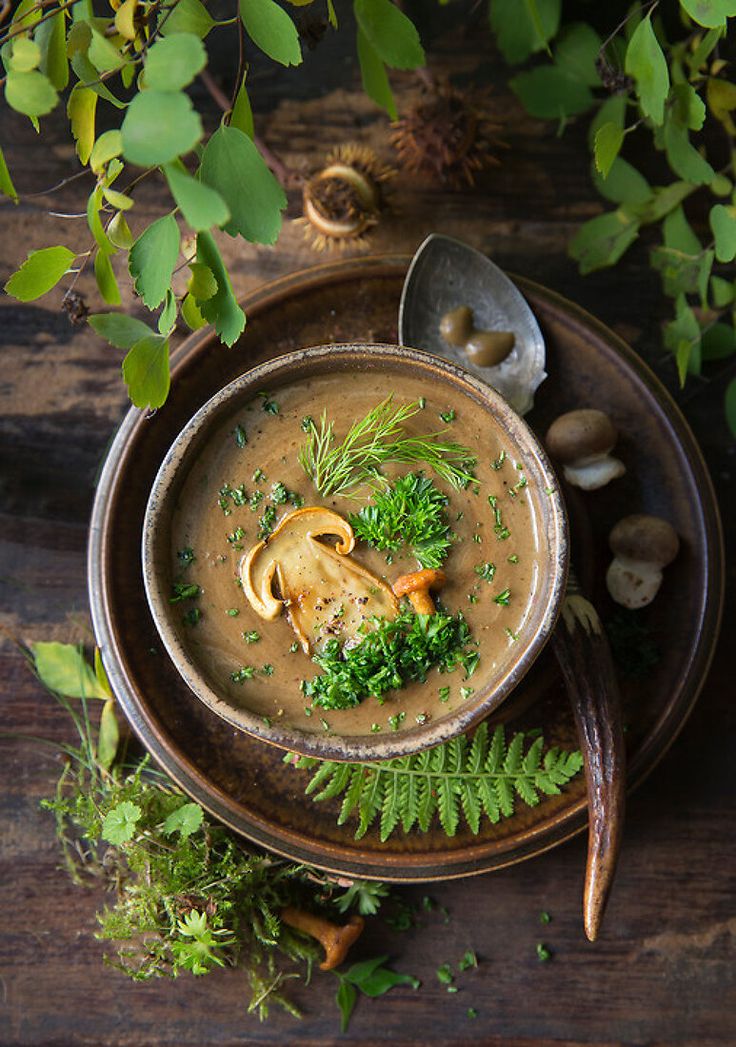 a bowl of soup with mushrooms, parsley and herbs on a wooden table next to spoons