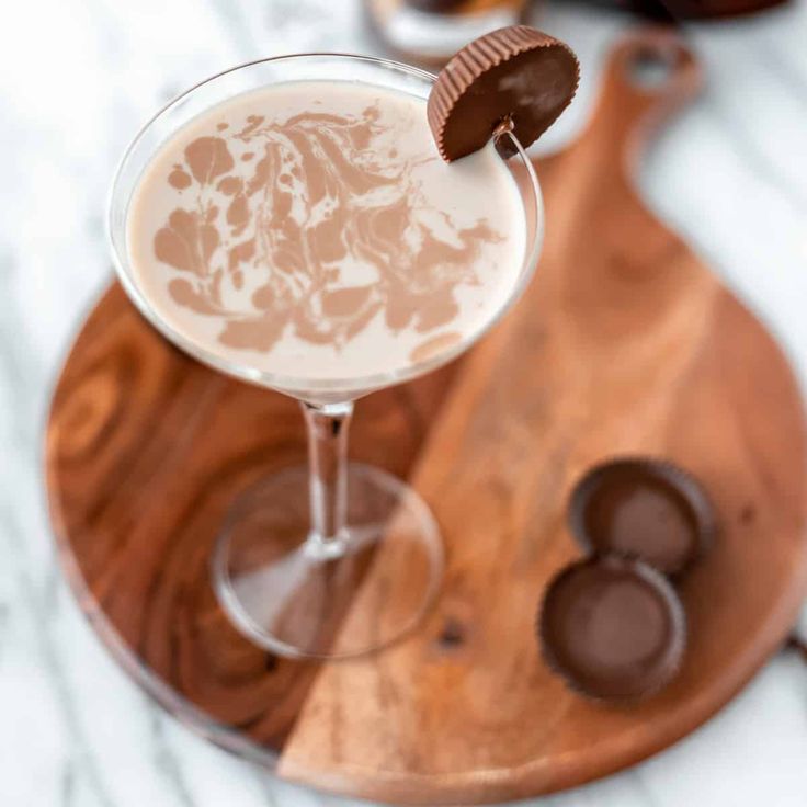 a chocolate covered drink in a glass on a wooden platter with some cookies and candy