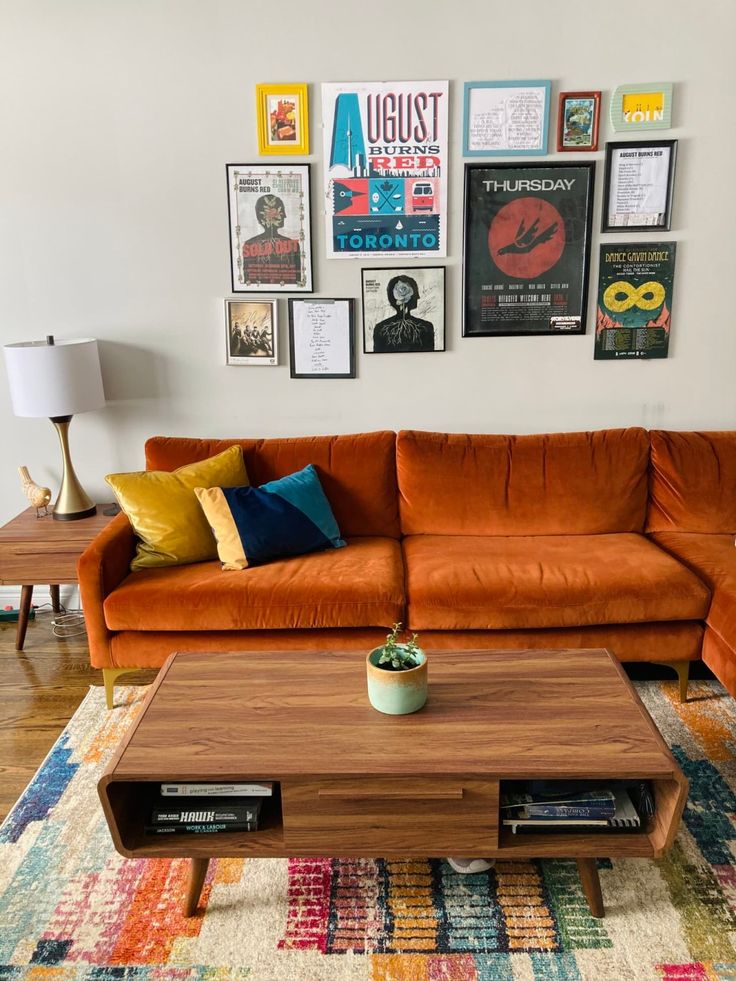 a living room with an orange couch and coffee table in front of pictures on the wall