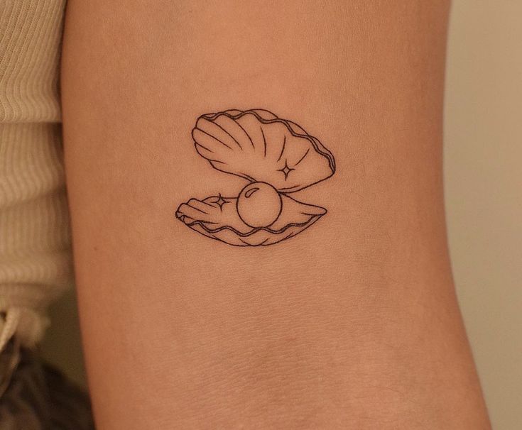 a woman's arm with a small shell tattoo on it