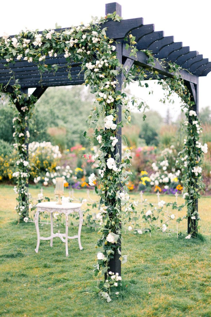 an outdoor wedding setup with white flowers and greenery on the arborette, table and chairs