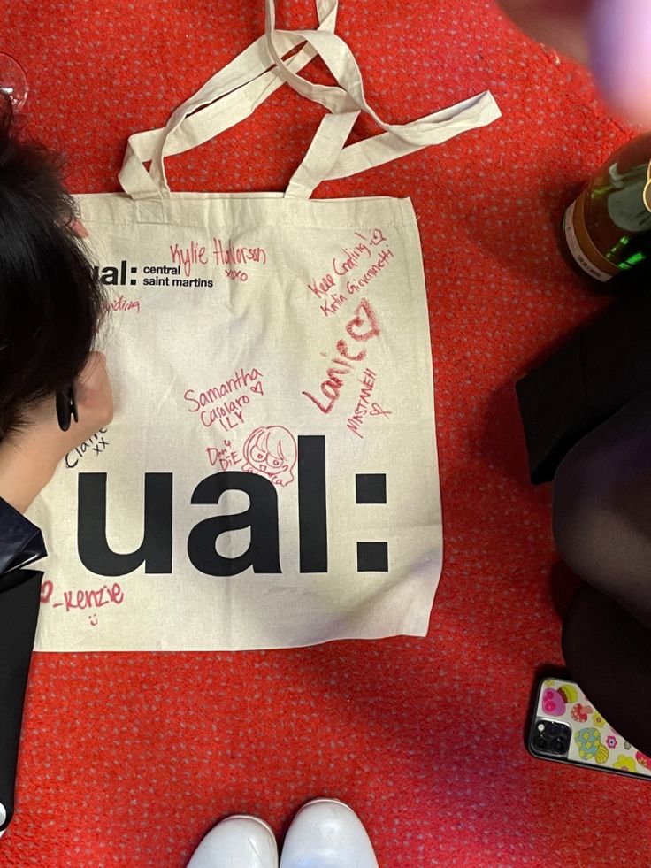 a woman sitting on the floor next to a bag with writing on it and shoes