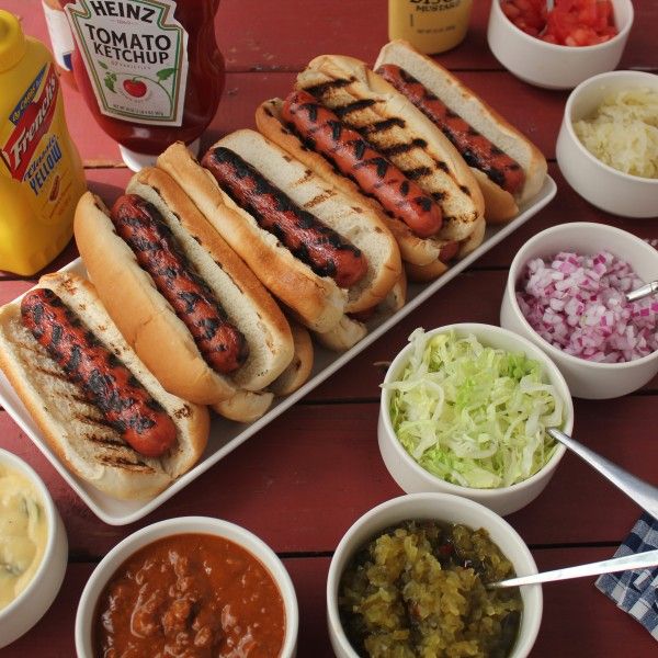 hotdogs and condiments on a picnic table with mustard, ketchup, onions, relish