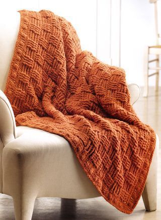 an orange knitted blanket sitting on top of a chair next to a white chair