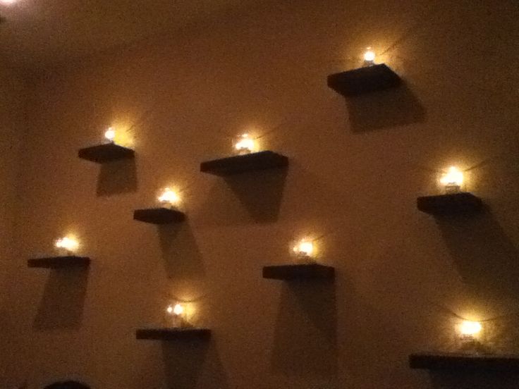 a room with several shelves and lights on the wall above them, all lit up by candles