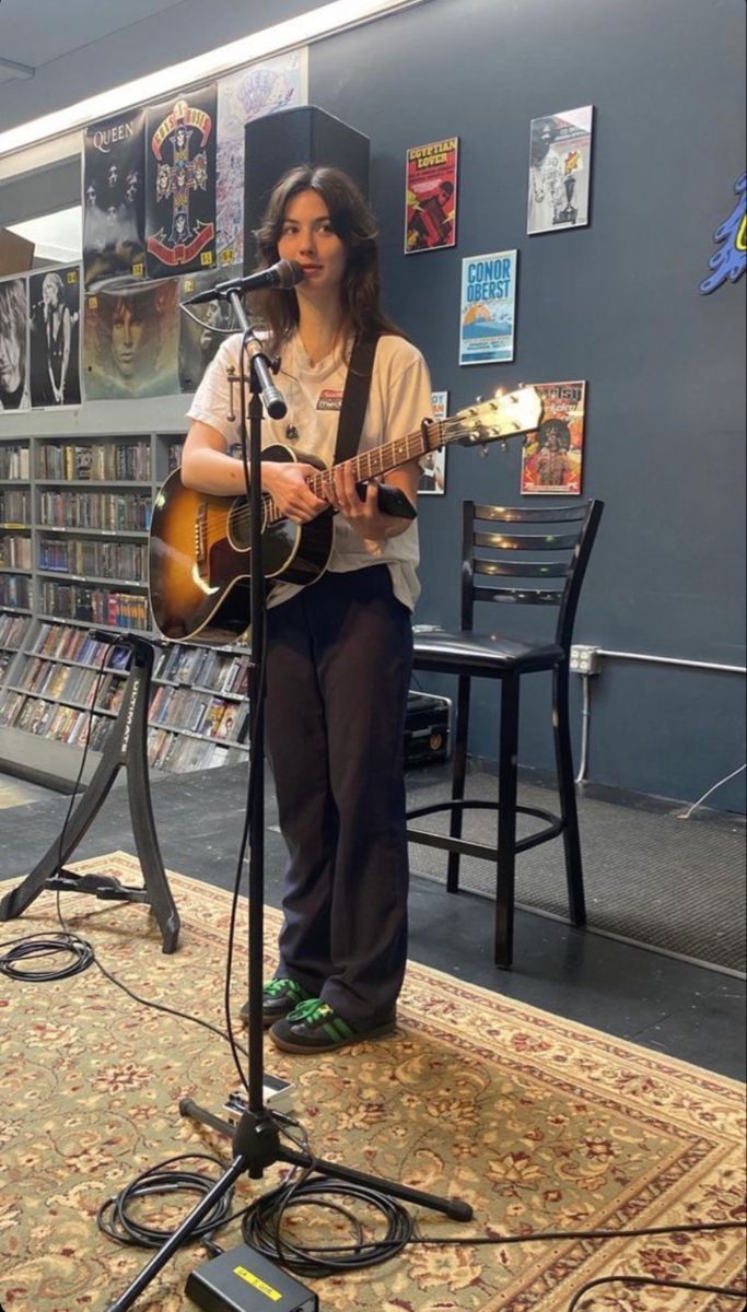 a woman standing in front of a microphone while playing an acoustic guitar and singing into a microphone