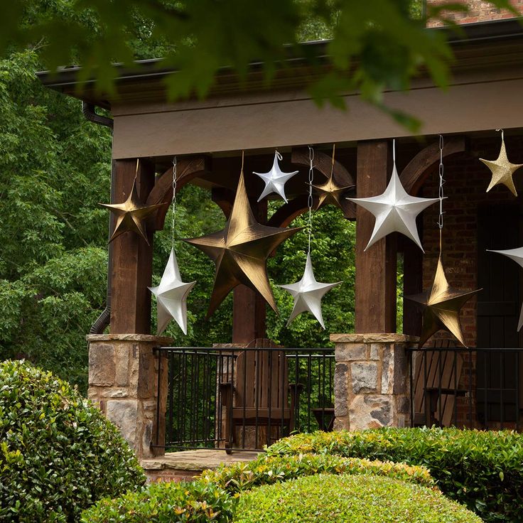 some white and gold stars hanging from the side of a building with trees in the background