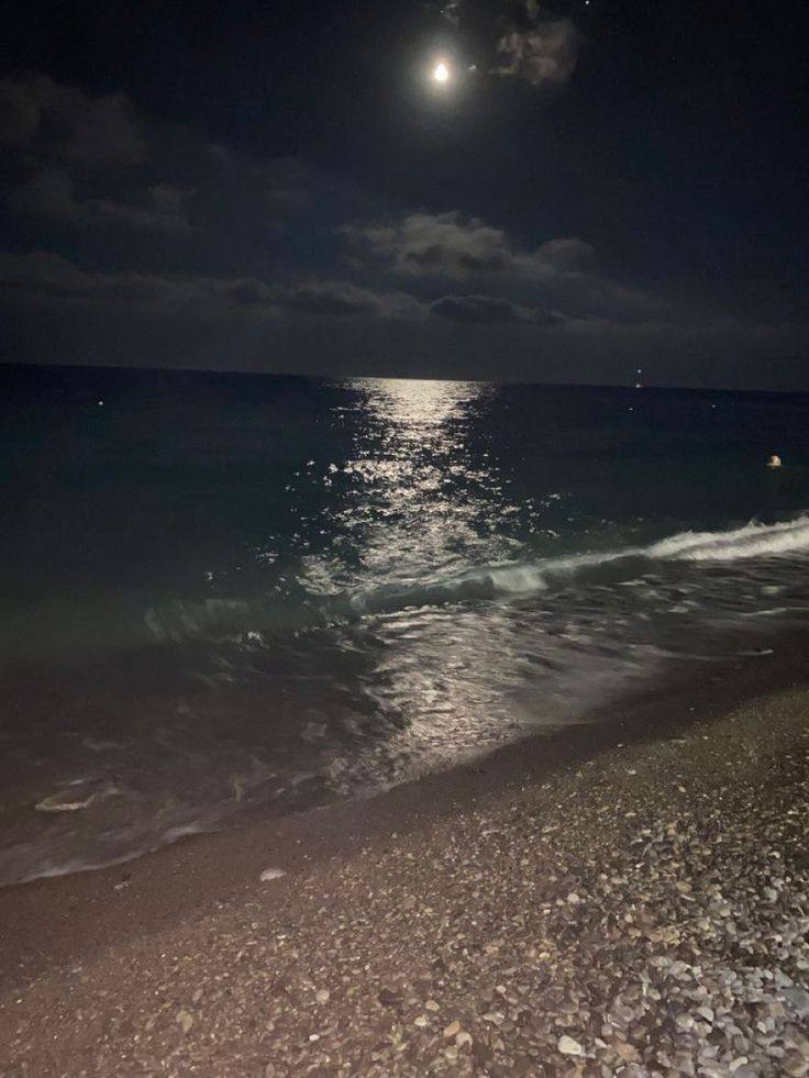 the moon is shining over the ocean at night