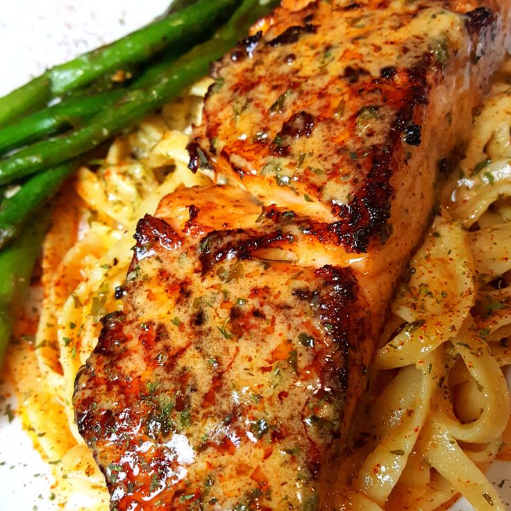 a piece of meat and some pasta on a white plate with asparagus next to it