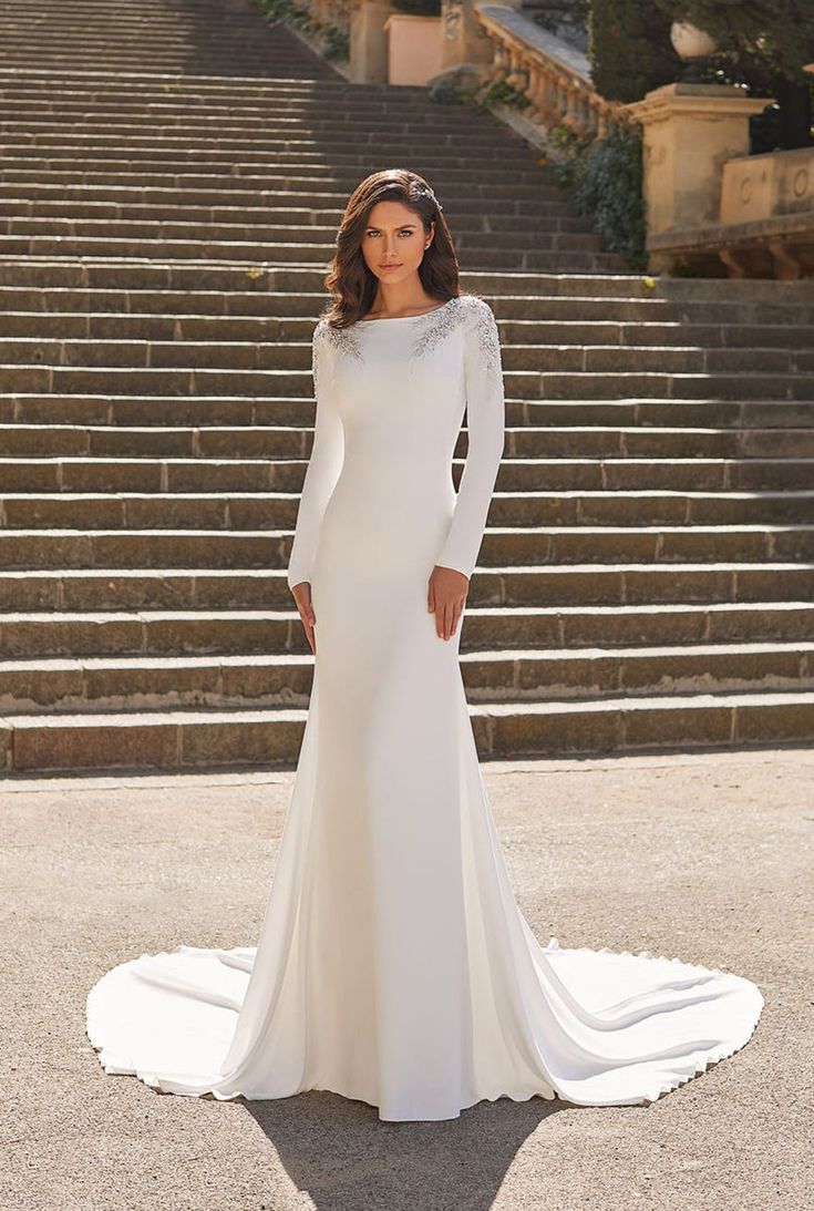 a woman standing in front of some steps wearing a long sleeved white wedding dress