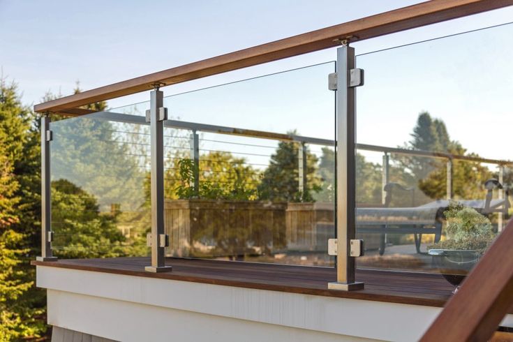 a wooden deck with glass railings and trees in the background