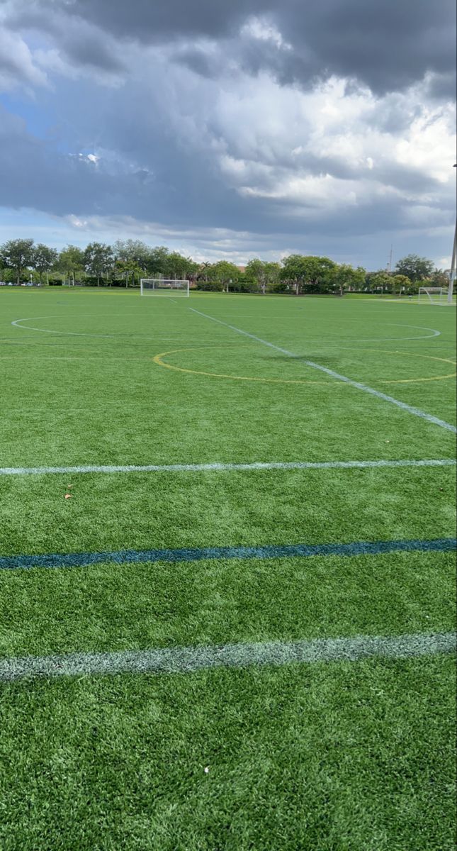 an empty soccer field with green grass and white lines on the ground under a cloudy sky