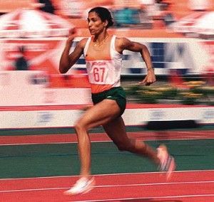 a woman running on a race track in front of an orange and white stadium audience