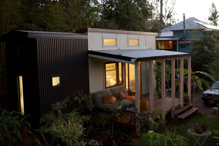 a small house sitting in the middle of a lush green field next to a forest