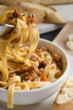 a spoon full of pasta with meat and cheese on the side next to bread slices