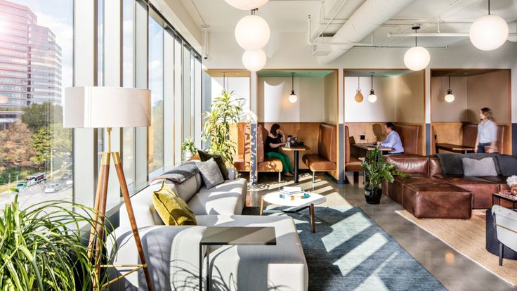 a living room filled with lots of furniture next to tall glass windows covered in sunlight